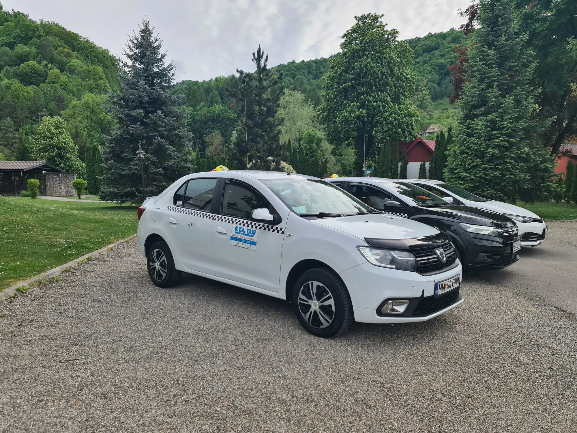 Taxi alb GTA Taxi Sighet cu semnul TAXI pe plafon, văzut din trei sferturi față.