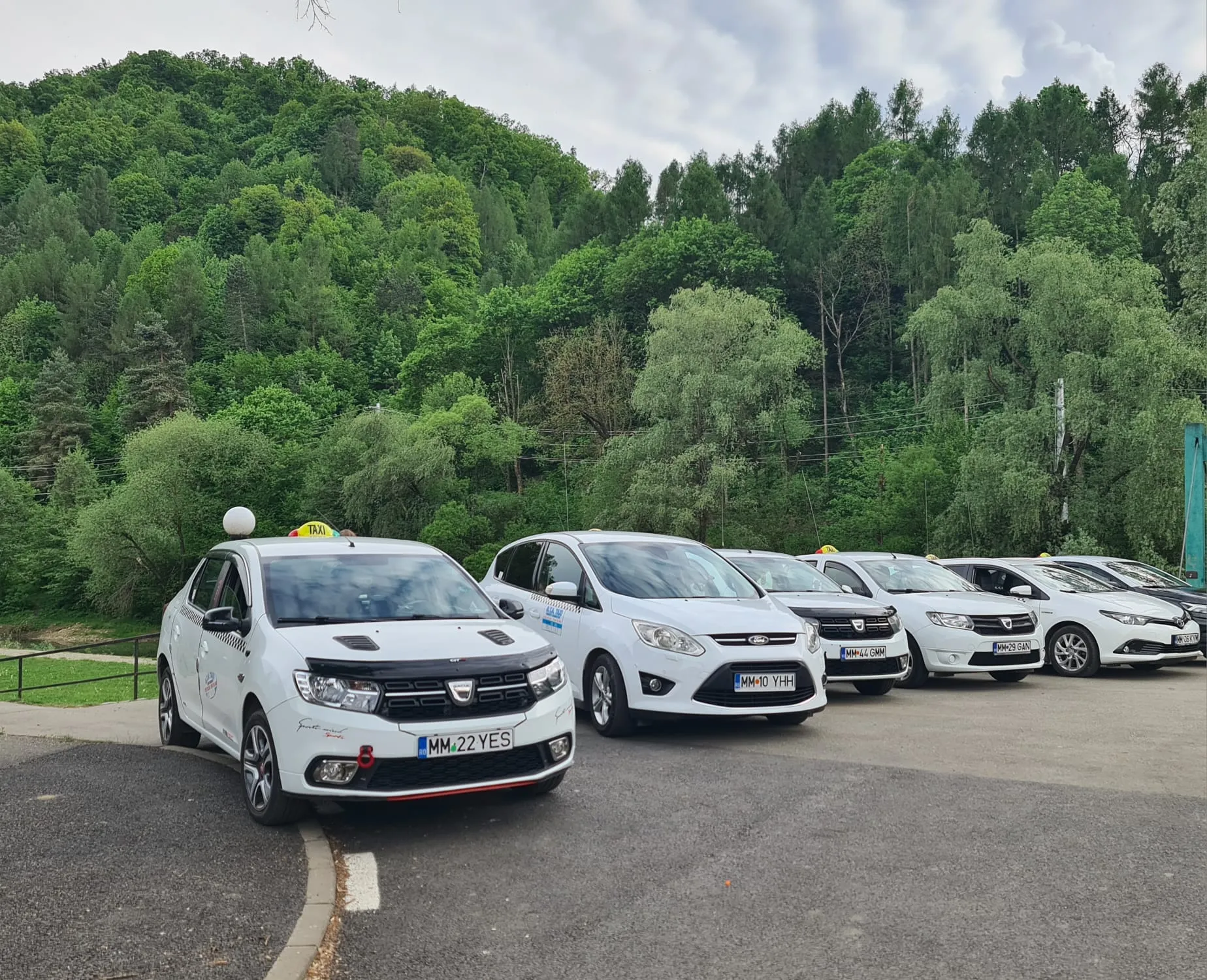 Taxi alb GTA Taxi Sighet cu semnul TAXI pe plafon, văzut din trei sferturi față.